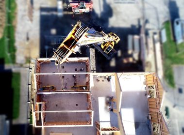 Suivi de chantiers par drone et autres types de caméras. Vue aérienne d'une grue au dessus d'un chantier. Ici une vue au nadir, d'une grue jaune en train d'approvisionner un chantier.