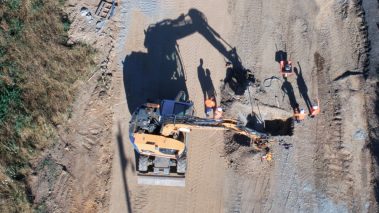 Une excavatrice creuse une tranchée. Des buses et autres conduits en béton y sont installés. Par la suite une machine télé-commandée passe pour aplanir et tasser le terrain