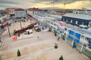 Suivi de chantier par drone à la gare du Mans. Prises de vues aériennes pour la filiale d'Engin, à savoir Axima, en charge de la réfection d'une partie des toitures. La photo a été prise depuis le parvis de la gare avec les services de sécurité. On y voit l'entrée de la gare ainsi que les fameux tramway oranges ainsi que les bus de la même couleur. A cette heure matinale le parvis de la gare est encore bien seul. Il faut dire que c'est l'a période des vacances, mais également d'une grève.