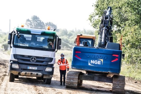 Deux véhicules de la société Guintoli, filiale de NGE, se rencontrent sur un chemin de terre en parallèle de la RN 165. Au milieu des deux engins, un homme masqué et casqué donne ses consignes.