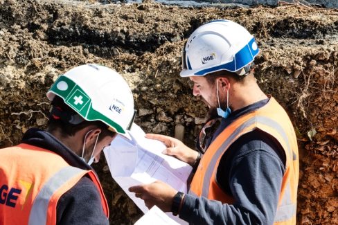 Deux ouvriers consultent les plans du projets dans une tranchée.