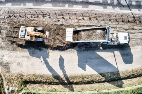Suivi de chantier aux abords de la RN 165, et son passage à 2X4 voies. Une pelle attend qu'un camion déverse le contenu de sa benne sur la voie avant de l'étaler et de commencer le tassement.