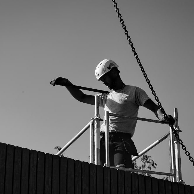 Un charpentier sur une toiture tient une masse en équilibre sur son épaule. Encore un reportage photo et suivi de chantier réussis pour Olao