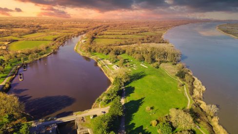 Prise de vue aérienne du canal de la Martinière au Pellerin près de Nantes. Le soleil se lève et les couleurs sont éclatantes. Du vert des prés baignés de lumière, aux teintes violacées du cours d'eau artificiel. Ce canal long de 15 kilomètres nous offre des chemins de halages qui permettent de belles et longues ballades à vélo. Des activités nautiques et de pêches sont aussi d'actualités. Cette partie du canal, la Loire est touche proche. Un restaurant y est ouvert une grande partie de l'année. Ce lieu est atypique avec ses deux bateaux en béton, ces civeliers, et son bateau mou de l'artiste Erwin Wurm. Cette œuvre nommée Misconceivable est visible toute l'année.