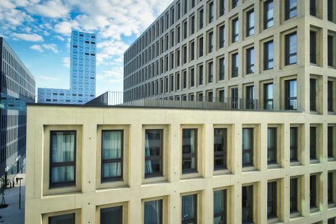 Prise de vue aérienne du nouveau quartier Polaris situé sur l'île de Nantes. Sur la droite de la photo, les dizaines de fenêtres de la résidence étudiante de 300 logements. Sur la gauche, l'école Vatel éclairé par le soleil qui se lève. Au milieu de la photographie s'élève la tour Polaris, perchée dans les nuages. Le ciel est très bleu et la lumière est rase. Deux personnes sont à l'entrée de l'école Vatel.