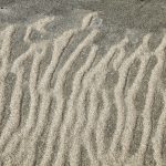 Sur un sable gris, témoin d'une basse mer, des lignes de sable plus fin et plus clairs se forment et parviennent à remonter la pente