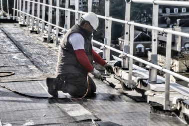 Un ouvrier étancheur est en train de souder une membrane bi-couche d'étanchéité sur une toiture à Angers. Il porte ses EPI, gants, lunettes, et protection-bouchon d'oreilles.