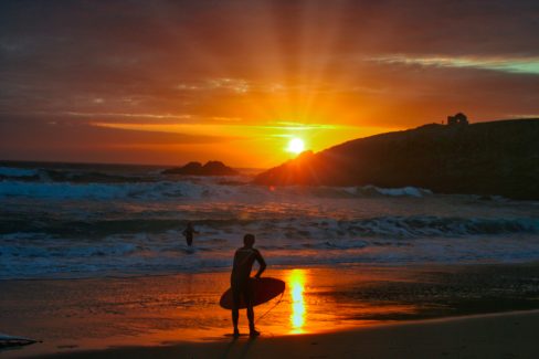 Une session de surf commence sur la presqu'île de Quiberon. le soleil se couche à proximité de la maison du douanier et donne un ciel aux couleurs orangers.