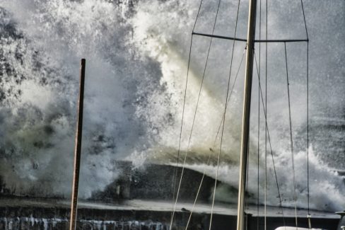Une vague monstrueuse passe par dessus la digue du port de Portivy en Bretagne. Les coques et mâts des bateaux subissent les assauts du vent et des éléments. La digue tient encore le coup après cette première tempête d'hiver.