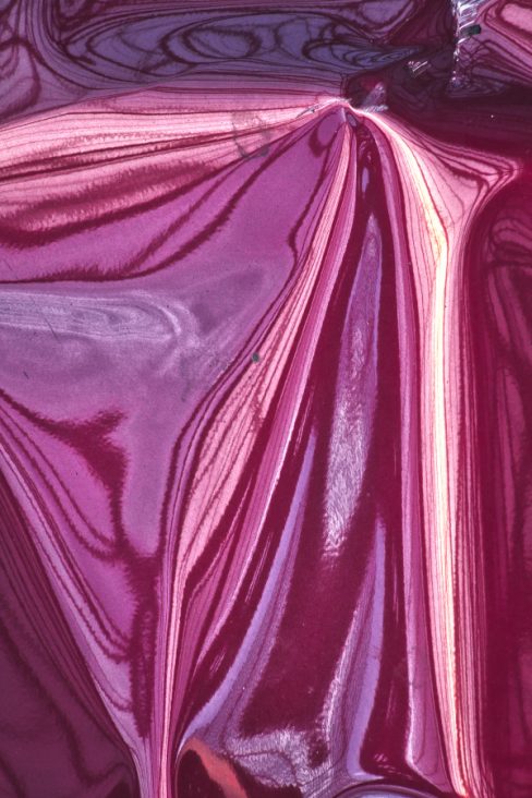 Dans cette parenthèse photographique, les couleurs parme et violette, et des lignes voluptueuses et blanches semblent couler, se renverser, comme si, une peinture acrylique se déversait sur le sol. Il s'agit en fait d'une carrosserie de voiture qui est tordue, le soleil se reflète par endroit.