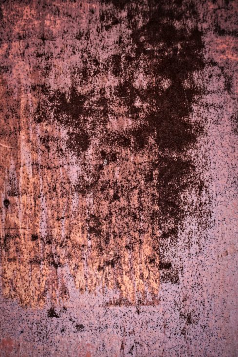 Un mur peint en rose est parsemé de tâches brunes, de multiples points d'impacts générés par le temps et qui ressemblent à de la corrosion.