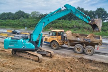 Une pelle de couleur bleu ciel est en train d'alimenter un chargeur positionné à ses côtés. D'énormes pierres sont arrachées du sol avant d'être chargées.