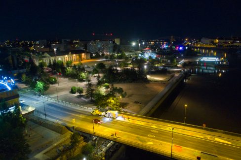 Deux camions de la société Esvia sont garés sur le Pont Anne de Bretagne. Ils sont en train de peindre les nouvelles pistes cyclables de ce pont. Au loin, le carrousel des mondes marins, et les anneaux de Buren viennent illuminés la nuit.
