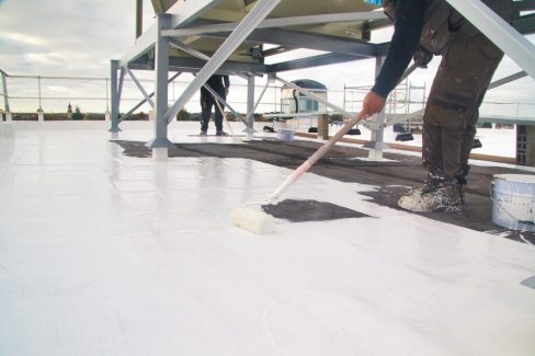 Un ouvrier passe une résine au rouleau. Il s'agit de la dernière étape d'un suivi de chantier ayant commencé 8 mois plus tôt: l'application d'une résine mono-couche sur l'étanchéité qui vient d'être refaite.