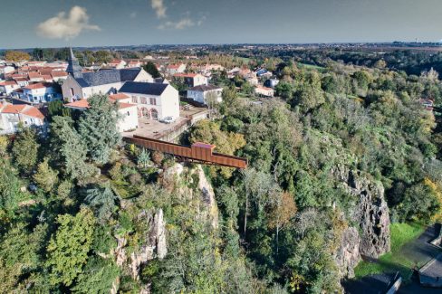 Vue aérienne de Château-Thébaud. Au second plan, son église et sa mairie, et au premier plan: le nouveau belvédère le "Porte-Vue" imaginé par Emmanuel Ritz et s'inscrivant dans le cadre du Voyage à Nantes vient d'ouvrir au public. De couleur rouille, il s'avance d'une vingtaine de mètres au dessus de la Maine et du site de Pont-Caffino connu pour le kayak et ses blocs d'escalade. Il invite à contempler la nature depuis la cime des arbres voire bien au-dessus.