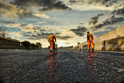 Photo-reportage de chantiers. Deux hommes habillés de orange réalisent des travaux de marquage et pré-marquage au sol. Cette opération est nécessaire avant de procéder au marquage définitif de ce nouvel échangeur à la Roche sur Yon.