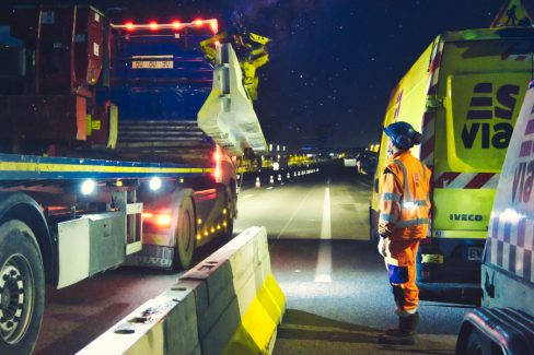 Photographies de nuit prise lors d'un suivi photographique et reportage de chantier nocturne. Un homme en orange de la société Esvia, attend qu'un camion muni d'une grue dépose une BT4- Il s'agit d'une glissière de sécurité destinée à séparer une voie en travaux de la route dite "normale". Pendant toute la nuit, ils vont déposer ces glissières en béton afin de faciliter les travaux de création d'une nouvelle voie en direction de Vannes. Les cônes orange sont de sortie.