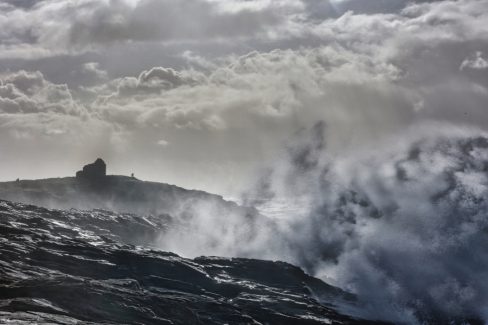 Photographie d'une tempête sur la côte sauvage de Quiberon dans le Morbihan. Le lieu-dit est appelé par les locaux la maison du douanier. Non loin, du trou du souffleur, une vague vient s'écraser contre la falaise. La quantité d'écume et d'embruns qui se disloquent dans le ciel commencent à cacher cette fameuse maison.