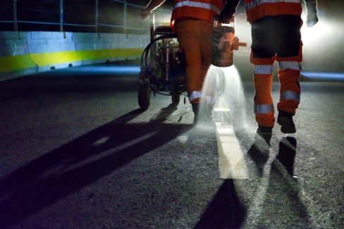 Un homme saupoudre un durcisseur juste après l'application d'une peinture de marquage au sol.