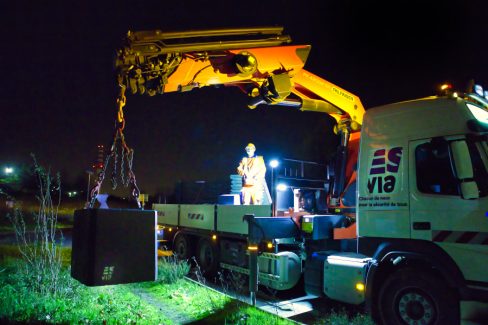photographies de nuit d'un homme muni d'une radiocommande guide une grue. cette grue jaune de type palfinder dépose un bloc en béton destiné à accueillir une pancarte provisoire signalant la présence d'un chantier