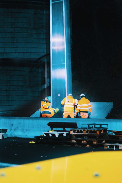 Des hommes en orange et casqués s'active au pied d'un portique qu'ils sont en train de fixer. Une opération très délicate.