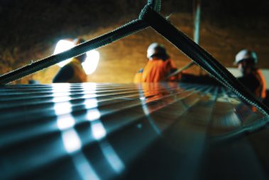 Une partie du portique est train d'être assemblée par des ouvriers casqués. Cette opération se déroule de nuit, les routes sont fermées à la circulation.