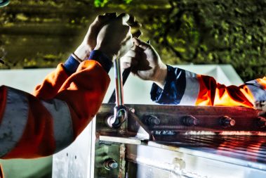 Photographies de nuit et suivi de chantiers de nuit réalisés lors d'un suivi de chantier en Vendée. Deux hommes en orange tiennent un outil entre leurs mains. Chacun a besoin de l'effort de l'autre. Ils ne peuvent y arriver que quand l'autre exerce une force. Des boulons de gros diamètres sont ainsi serrer manuellement.