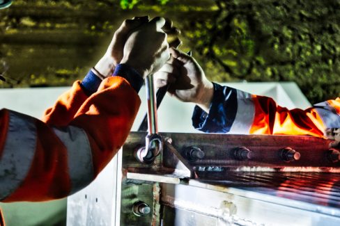 Photographies de nuit et suivi de chantiers de nuit réalisés lors d'un suivi de chantier en Vendée. Deux hommes en orange tiennent un outil entre leurs mains. Chacun a besoin de l'effort de l'autre. Ils ne peuvent y arriver que quand l'autre exerce une force. Des boulons de gros diamètres sont ainsi serrer manuellement.