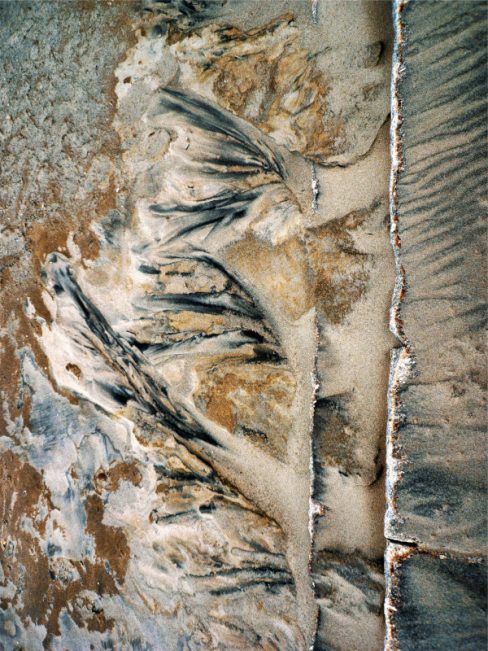 Du sable de plusieurs couleurs dévalent trois marches dans un escalier pour retrouver la plage.