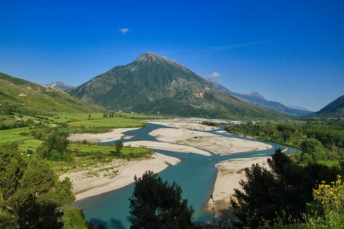 Destination Albanie pour cette fois. Au bord de la route menant à Burrit, un fleuve sillonne la vallée. L'eau est limpide et au centre de cette photographie trône une montagne. Le ciel est d'un bleu méditerranéen