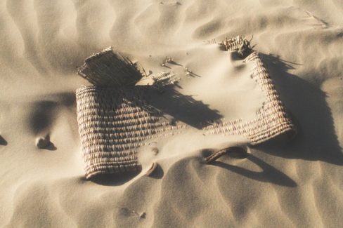 Un vieux sac tissé, fait main, est en train d'être dégradé par le vent et les grains de sable qui lui roulent dessus