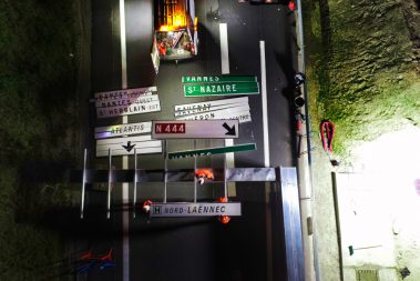 Suivis de chantiers routiers en photos. Des pancartes de signalisations sont en cours de montage sur une potence posée au sol. La prise de vue nocturne par drone est régie par certaines règles quant aux vols par drone.