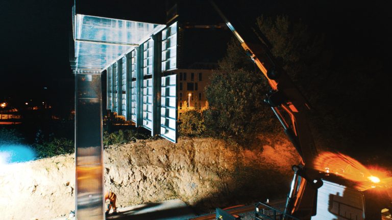 Vue de profil d'une potence directionnelle. Au sol, les hommes casqués sont en train de serrer les vis et les boulons.