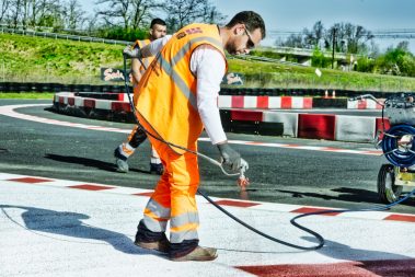 Un chef de chantier applique sur un fond blanc une couche de peinture rouge au pistolet à peinture. Ils sont en train de repeindre une piste de karting aux alentours de Tours. cette photo a été prise lors d'un suivi et reportage de chantier en Avril 2021