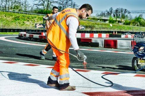 Un chef de chantier applique sur un fond blanc une couche de peinture rouge au pistolet à peinture. Ils sont en train de repeindre une piste de karting aux alentours de Tours. cette photo a été prise lors d'un suivi et reportage de chantier en Avril 2021