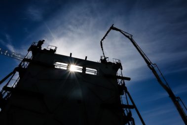 Photographie prise lors d'un suivi de chantier en Vendée par Thierry Duclos, photographe chantier. Il s'agit ici d'un contre jour au pied d'un mur en construction. Un camion pompe alimente des banches de 12 mètres de haut. Ces murs matricés vont être impressionnants