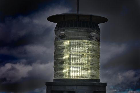Photographie de la balise d'une éolienne. Cette balise signale aux aéronefs la présence d'une éolienne. L'éclat de lentille transperce les nuages sombres de la Normandie