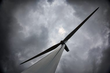 Au pied d'une éolienne. Le ciel est sombre et chargé. Il faut maintenant arrêter les moteurs et les pales de ce moulin à vent. Car , en effet, nous devons en faire l'ascension.