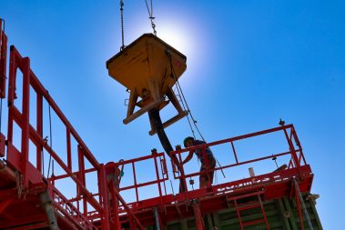 Un ouvrier casqué est en train de réceptionner du béton à couler. Ce béton se veut être décarboné.