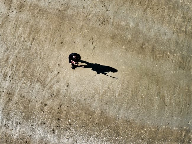 Un guitariste marche sur la plage. La photographie prise par drone lors d'un tournage. Et oui, car chez Olao ça tourne. Clip vidéo et films institutionnels