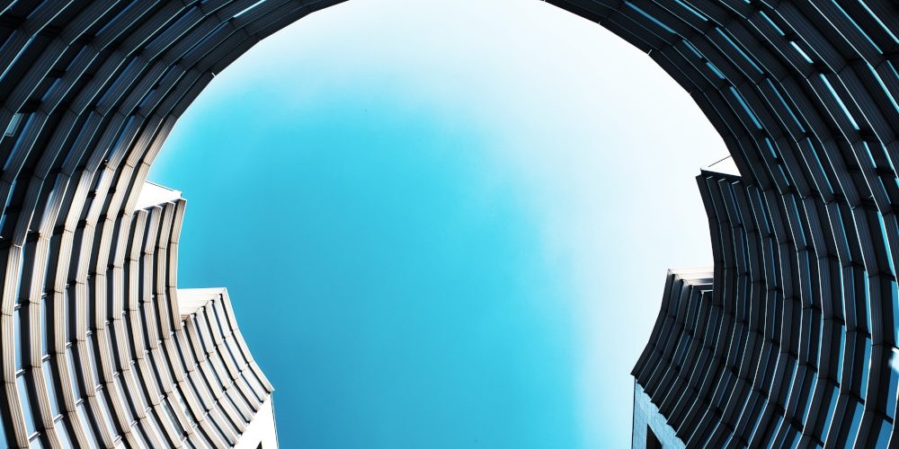 Photographe d'architecture. Au coeur d'un nouveau quartier d'affaires sur l'Ile de Nantes, les immeubles s'amusent à jouer avec les formes et le ciel. Ici, un immeuble en demi-cercle d'aspect métallique et froid semble enfermé un ciel bleu turquoise