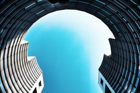 Photographe d'architecture. Au coeur d'un nouveau quartier d'affaires sur l'Ile de Nantes, les immeubles s'amusent à jouer avec les formes et le ciel. Ici, un immeuble en demi-cercle d'aspect métallique et froid semble enfermé un ciel bleu turquoise