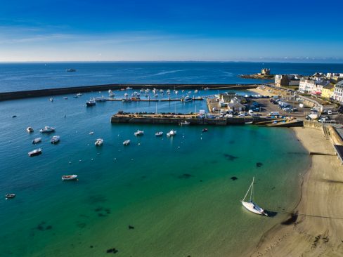 Vue aérienne de Port-Maria à Quiberon. Quelques bateaux de pêche sont amarrés. Au fond dans un ciel d'un bleu intense on distingue Belle-île en Mer et le château Turpault. L'eau est translucide et oscille entre le vert et le bleu. Les Caraïbes ? Non la Bretagne