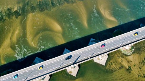 prise de vue aérienne de cinq voitures colorées sur un pont de Pierre aux Ponts de Cé dans le Maine et Loire. Le pont en diagonal traverse le Maine. A chaque pied de pont du sable et des sédiments se sont accumulés. Des arénaglyphes sont dessinés par ces sédiments et donnent un côté très graphique à cette photographie prise par drone.