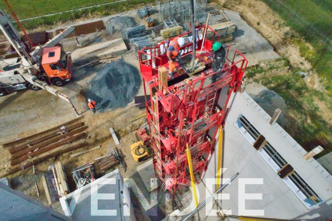 Prises de vue par drone lors d'un suivi de chantier. Trois hommes casqués sont en train de couler du béton décarbonné dans des banches hautes de plusieurs mètres.