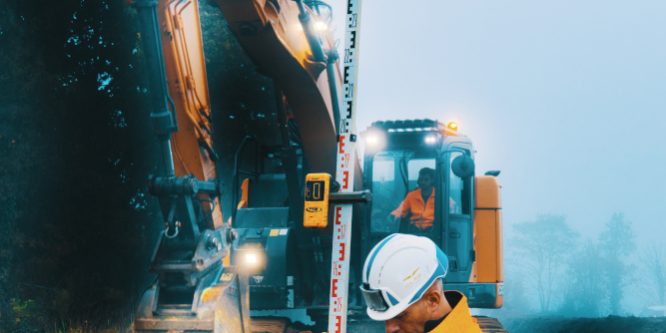C'est en tant que photographe chantier que nous sommes intervenus sur ce suivi. Un homme en orange et casqué est en train de vérifier à l'aide d'un laser si la tranchée que la pelle en second plan est suffisamment profonde pour accueillir des tuyaux destinés à transporter de l'eau potable.