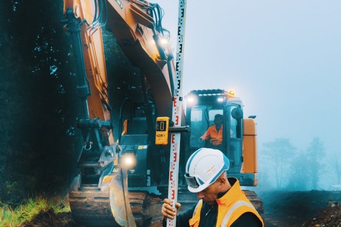 C'est en tant que photographe chantier que nous sommes intervenus sur ce suivi. Un homme en orange et casqué est en train de vérifier à l'aide d'un laser si la tranchée que la pelle en second plan est suffisamment profonde pour accueillir des tuyaux destinés à transporter de l'eau potable.