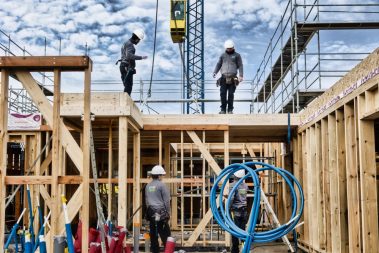 Une équipe de charpentiers de l'Atelier Isac s'organise lors d'un levage XXL. Un binôme est à l'étage, et l'autre en bas afin de réceptionner des panneaux de toitures