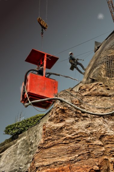 Deux hommes d'une entreprise de cordistes sont en train de mètre en place du béton projeté.