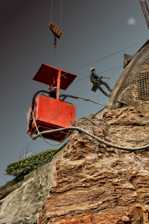 Deux hommes d'une entreprise de cordistes sont en train de mètre en place du béton projeté.